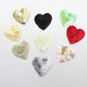 Peut inclure: Un assortiment de patchs en forme de cœur ornés de paillettes de différentes couleurs : or, noir, vert, rouge, blanc et argent. Les paillettes sont disposées pour créer un effet texturé et scintillant, idéal pour embellir des vêtements ou des créations artisanales.
