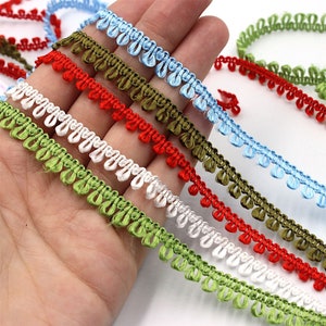 Könnte beinhalten: Sortiment an bunten Besätzen mit einer geschlungenen Franse. Die Besätze sind in Rot, Grün, Weiß und Blau erhältlich.