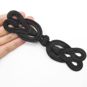 Könnte beinhalten: Schwarze geknotete Schnur-Toggle-Verschluss, ein traditioneller chinesischer Knopf, mit zwei Schlaufen an jedem Ende.