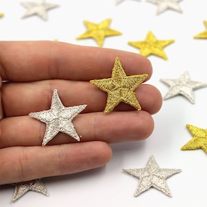 May include: A collection of gold and silver star-shaped fabric patches. The patches are embroidered with a metallic thread and have a shiny finish.