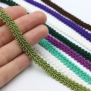 May include: Assortment of decorative trim in various colors, including green, white, teal, purple, and dark green. The trim features a delicate, repeating pattern of loops and swirls.