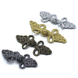 Könnte beinhalten: Vier dekorative chinesische Knoten-Verschlüsse in Silber, Gold und Schwarz. Die Verschlüsse haben die Form eines Knotens mit einer Schlaufe an jedem Ende.