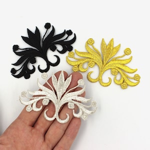 Może przedstawiać: Trzy haftowane naszywki do prasowania w kształcie stylizowanego wzoru kwiatowego. Naszywki są czarne, złote i srebrne.