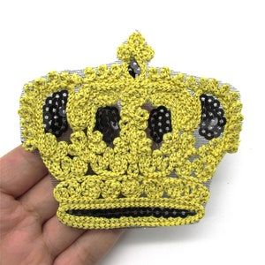 Puede incluir: Un parche de corona de lentejuelas amarillas y negras. La corona está hecha de tela de crochet con lentejuelas cosidas.