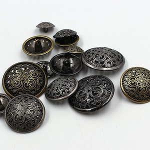 May include: Assortment of decorative metal buttons with intricate designs. The buttons are in shades of gold and black with a variety of patterns.