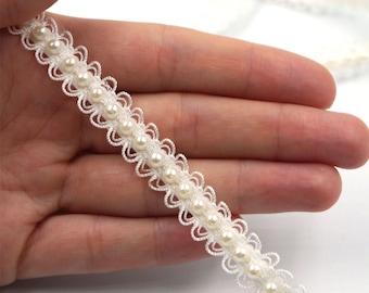 Può includere: Bordino di perline bianche con un delicato motivo floreale. Il bordino presenta piccole perle bianche cucite su una base di pizzo bianco.