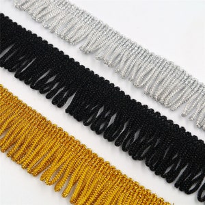 May include: Three strands of fringe trim in gold, black, and silver. The fringe is made of a soft, textured material.