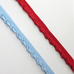 May include: Two strips of decorative gimp trim, one in a bright red and the other in a light blue. Each trim features a central woven cord flanked by a series of small, uniform, slanted loops along one edge, creating a consistent textured pattern.