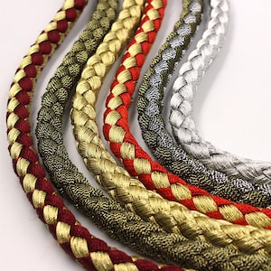 Puede incluir: Cinco cordones trenzados en diferentes colores, incluyendo rojo, dorado, plateado y verde. Los cordones están tejidos con un hilo metálico, lo que les da un aspecto brillante.