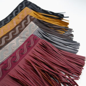 May include: Assortment of six leather fringe trims with a wavy design. The trims are in various colors, including black, brown, gray, red, and yellow.