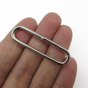 May include: A silver-toned metal oval ring connector with a smooth, polished finish. The hardware features a continuous, elongated loop design with a single visible seam where the two ends meet, creating a sturdy and functional component.