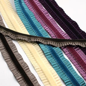 May include: A selection of velvet ribbon trim in a range of colours: brown, cream, teal, purple, and deep purple. Each ribbon has a ruffled edge, adding a textured, decorative element. Suitable for sewing and craft projects.