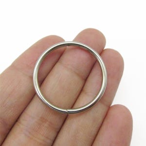 May include: A smooth, circular metal ring with a polished silver-toned finish. The ring features a simple, continuous design with a single visible seam where the two ends meet, creating a clean and uniform appearance for various craft applications.