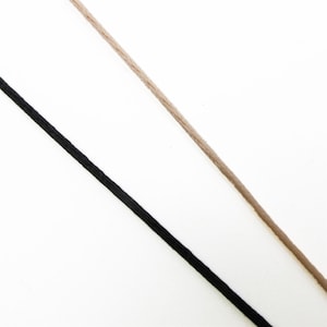 May include: Two thin, smooth cords positioned diagonally across the frame. One cord is solid black, and the other cord is a light tan or beige colour. Both cords appear to be made of a tightly woven, rounded material with a consistent thickness.