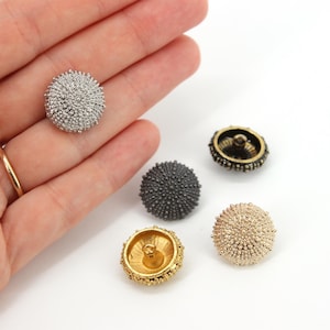 May include: A collection of five round, textured buttons with a domed, spiky surface resembling sea urchins. The buttons are finished in metallic silver, matte dark grey, antique bronze, and gold tones, each featuring a central shank loop.
