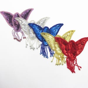 Puede incluir: Colección de cinco apliques de mariposa con lentejuelas en morado, plateado, azul, dorado y rojo. Cada mariposa tiene flecos de cuentas. Los apliques se muestran sobre un fondo blanco. Adecuados para adornar ropa o accesorios.