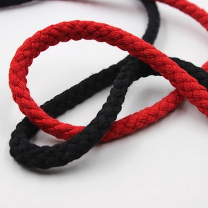 May include: Close-up of two braided cords, one black and one red. The cords are twisted together, showing the texture of the braided material.