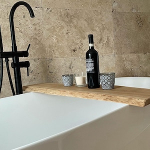 Puede incluir: Una bandeja de baño de madera con una botella de vino, dos velas y dos candelabros decorativos. La bandeja está colocada en el borde de una bañera blanca.