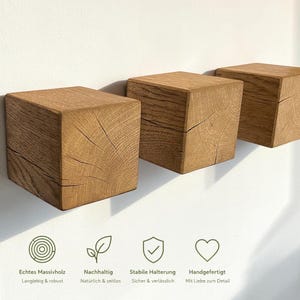 Könnte beinhalten: Drei Wandhaken aus hellbraunem Holz in Würfelform mit sichtbarer Maserung und natürlichen Rissen. Unter den Haken befinden sich vier Symbole mit dem Text: Echtes Massivholz, Langlebig & robust, Nachhaltig, Natürlich & zeitlos, Stabile Halterung, Sicher & verlässlich, Handgefertigt, Mit Liebe zum Detail.