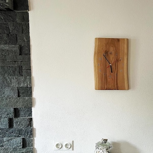May include: A wooden clock with black hands and a red second hand. The clock face has black numbers on a light wood background. The clock is mounted on a light wood wall.