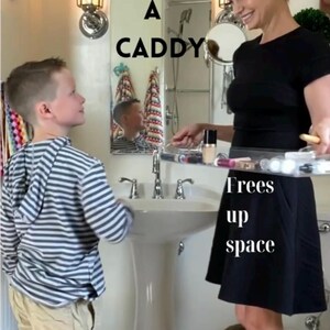 May include: A clear acrylic bathroom caddy holding various cosmetic bottles and tubes. The text USE A CADDY is printed in black above the caddy, and the text Frees up space is printed in white below the caddy, highlighting its storage function.