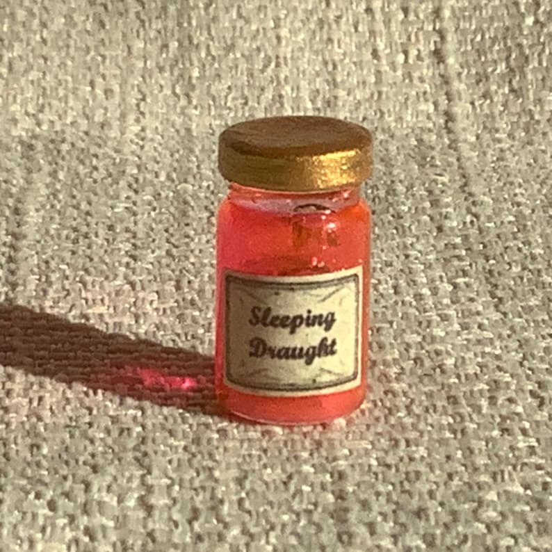 May include: A small glass jar with a gold lid filled with a pink liquid. The jar has a label that reads "Sleeping Draught".