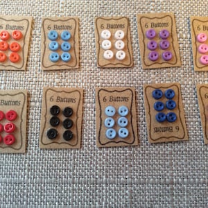 May include: Assortment of six packs of buttons in various colours, including red, white, blue, black, and purple. Each pack has a brown card with the text "6 Buttons" printed on it.
