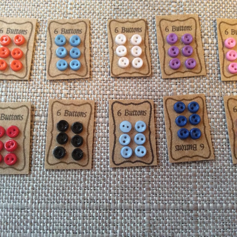 May include: Assortment of six packs of buttons in various colours, including red, white, blue, black, and purple. Each pack has a brown card with the text "6 Buttons" printed on it.