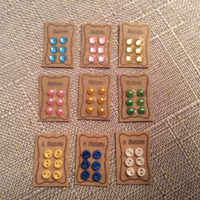 May include: Nine cards, each displaying six buttons in different colours. The colours include blue, pink, yellow, green, and white. Each card has the text "Buttons" or "6 Buttons" printed on it.