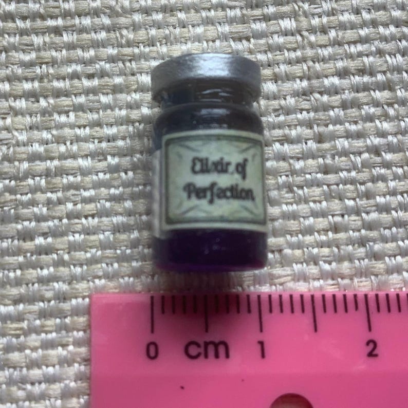 May include: A small glass bottle with a silver lid filled with a dark purple liquid. The bottle has a label that reads "Elixir of Perfection".