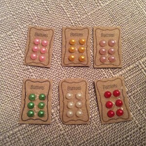 May include: Six cards with the word "Buttons" printed on them. Each card has six small round buttons in different colours: pink, yellow, white, green, and red.