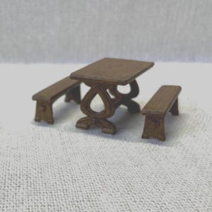 Peut inclure: Un ensemble de table et de bancs miniatures en bois. La table a un motif sculpté et les bancs sont simples et rectangulaires.
