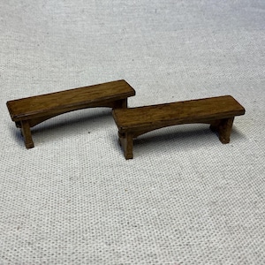 Puede incluir: Dos bancos de madera con un diseño sencillo. Los bancos son de madera marrón oscuro y tienen una parte superior ligeramente curvada. Ambos están sobre una superficie texturizada gris claro.