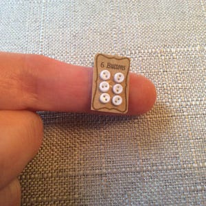 May include: A small card with the text "6 Buttons" printed on it. The card is brown and has six white buttons attached to it.