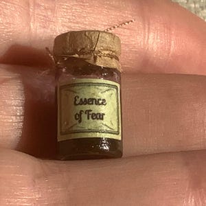 May include: A small glass jar with a cork lid and a label that reads "Essence of Fear". The jar is filled with a dark liquid.