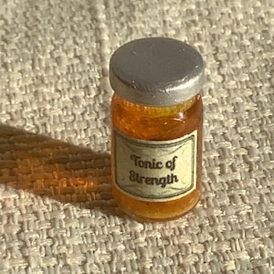 May include: A small glass jar with a silver lid filled with a golden liquid. The jar has a label that reads "Tonic of Strength".