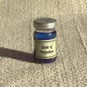 May include: A small glass bottle with a silver lid filled with a blue liquid. The bottle has a label that reads "Elixir of Perfection".