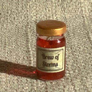 May include: A small glass jar with a gold lid filled with a red liquid. The label on the jar reads "Brew of Storms".