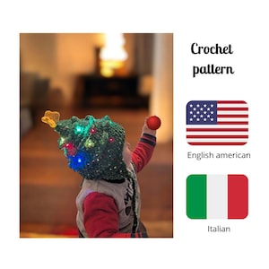 Può includere: Un cappello all'uncinetto verde a forma di albero di Natale con luci colorate e una stella gialla in cima. La persona indossa un ornamento rosso. L'immagine include il testo "Crochet pattern".