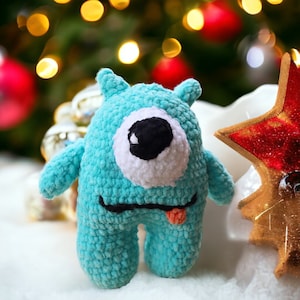 Può includere: Un giocattolo mostro in crochet blu turchese con un solo occhio bianco e una pupilla nera. Il mostro ha la lingua rosa che sporge ed è seduto su una superficie bianca.