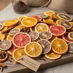 May include: A wooden cutting board displays a collection of dried citrus slices, including oranges, grapefruits, and limes. Cinnamon sticks and star anise are scattered among the fruit. A tag reads "Hand-Dried Citrus Blends."