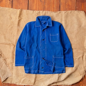 May include: A vibrant blue long-sleeve jacket featuring a classic collar, a single chest pocket, and two lower front pockets. The garment is constructed with visible white contrast stitching along the seams, pockets, and collar, and includes dark buttons.