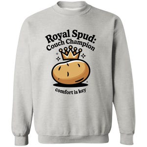 May include: A light grey sweatshirt featuring a cartoon potato wearing a crown. The text reads "Royal Spud: Couch Champion" above the potato and "comfort is key" below. The design is in black, brown, and gold.