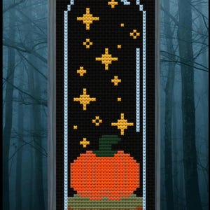 May include: A cross-stitch pattern of a pumpkin inside a glass jar with stars. The jar is outlined in white and the pumpkin is orange with a green stem. The background is black.