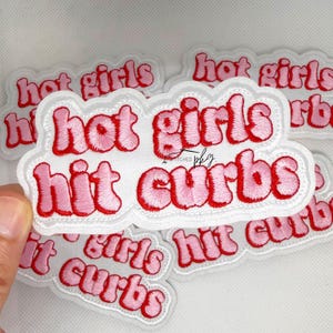 Puede incluir: Un parche bordado blanco con borde festoneado que presenta el texto rosa 'hot girls hit curbs' en una fuente redondeada y tipo burbuja. Las letras tienen un contorno rosa oscuro y el parche se muestra sobre un fondo liso y claro.