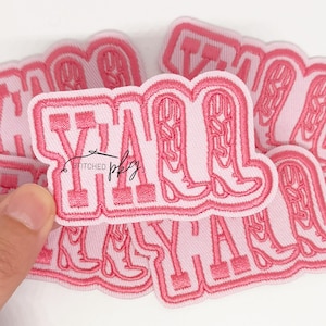 May include: Pink embroidered patch with the word "Y'all" and cowboy boots. The patch has a white background and a pink border. The text "stitched pby" is also visible on the patch. Several patches are visible.