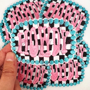 Puede incluir: Un conjunto de parches bordados con la palabra "HOMEY" en rosa. Cada parche tiene un fondo a cuadros blanco y negro, un borde festoneado y un ribete turquesa.