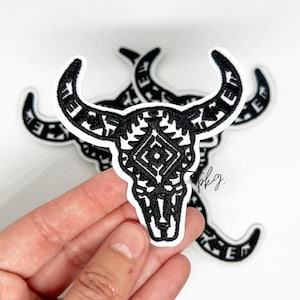 May include: Black and white embroidered iron-on patch of a bull skull with a geometric pattern.