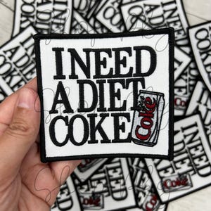 Puede incluir: Parche blanco para planchar con texto negro que dice "Necesito una Coca-Cola light" y una lata roja y blanca de Coca-Cola light.