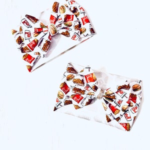 May include: Two white fabric headbands with a bow. The fabric has a pattern of fast food items, including chicken nuggets, sandwiches, and drinks. The pattern is in red, yellow, and brown.